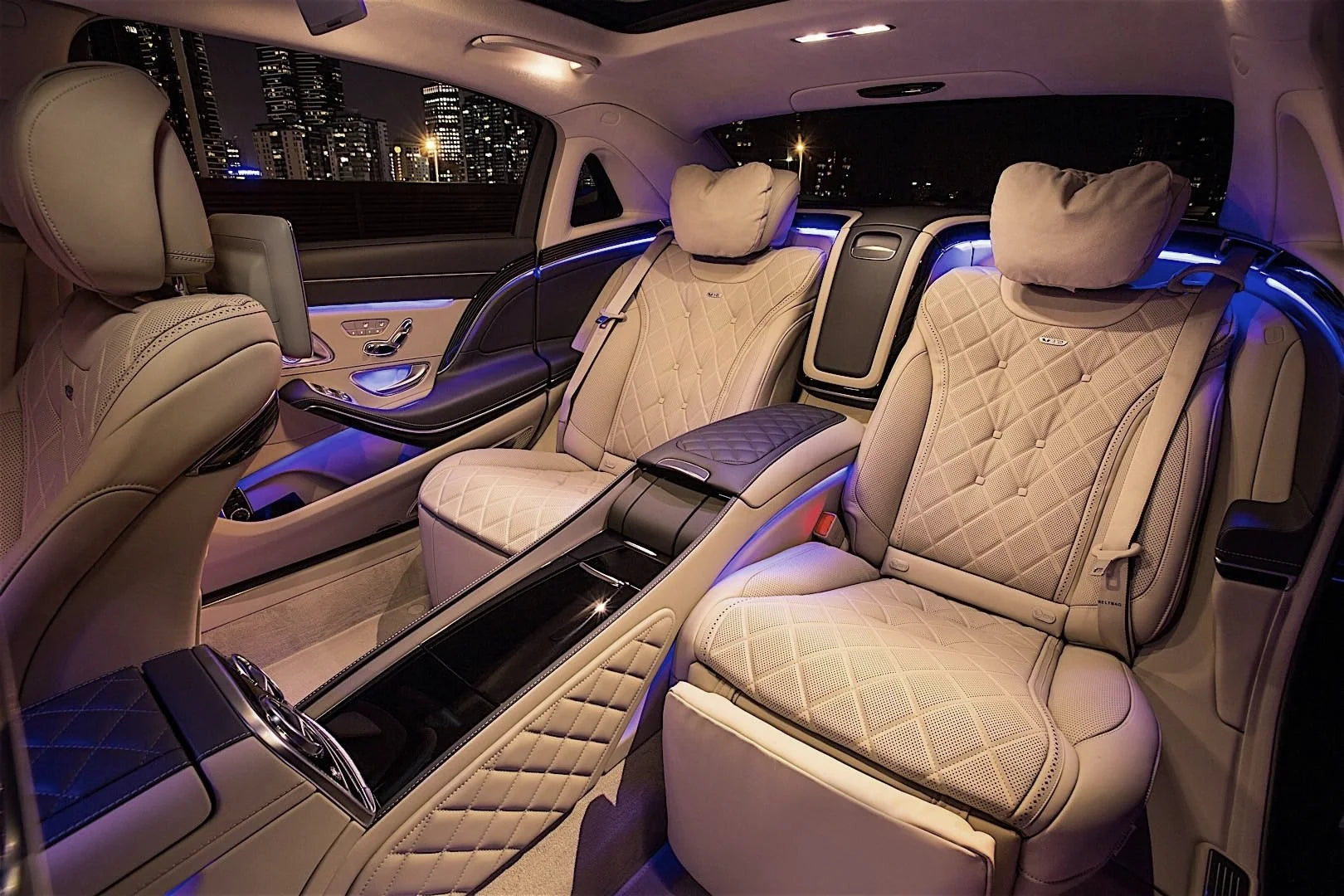The rear cabin of a chauffeured car at night, with two cream leather seats